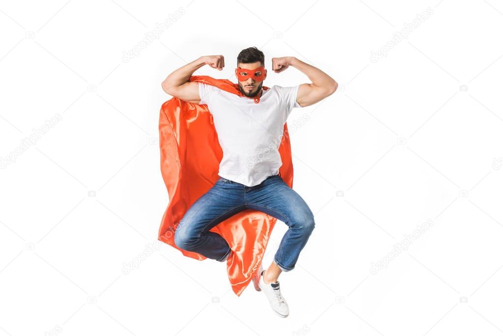 handsome young man in red cloak and mask looking at camera and showing muscles isolated on white 