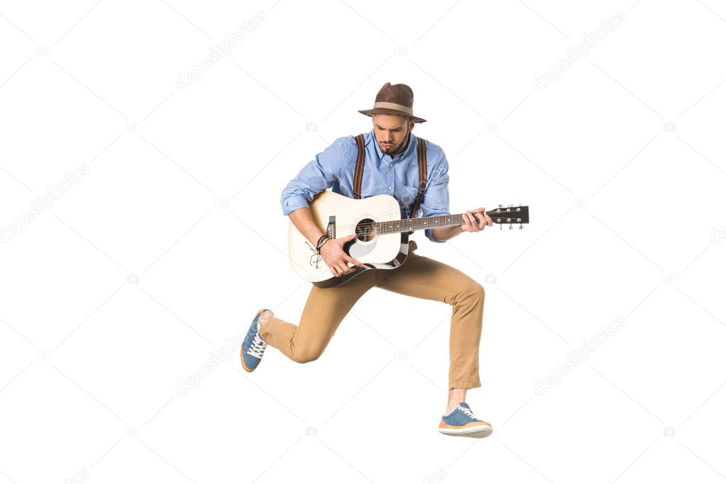 handsome young musician in hat playing guitar and jumping isolated on white 