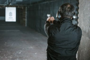 rear view of man aiming gun at target in shooting range