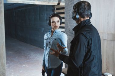 female customer talking with male instructor in shooting range  clipart