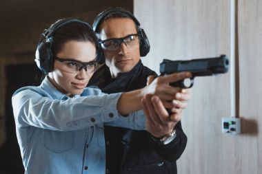 male instructor helping attractive female customer holding gun  clipart