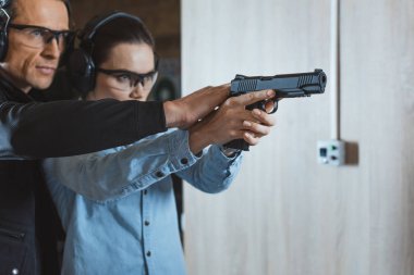 male instructor helping customer to shoot with gun in shooting range clipart