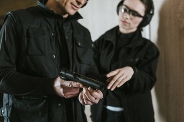 cropped image of instructor showing gun to female client in shooting gallery clipart
