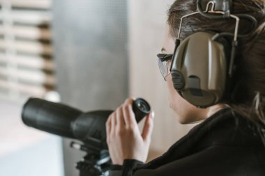 side view of woman with binoculars in shooting range clipart