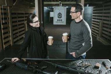 smiling customer and shooting instructor drinking coffee in shooting range clipart