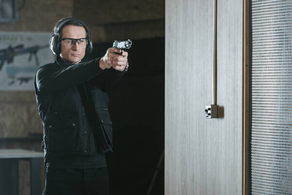 красавчик нацеливает пистолет на мишень в тире
