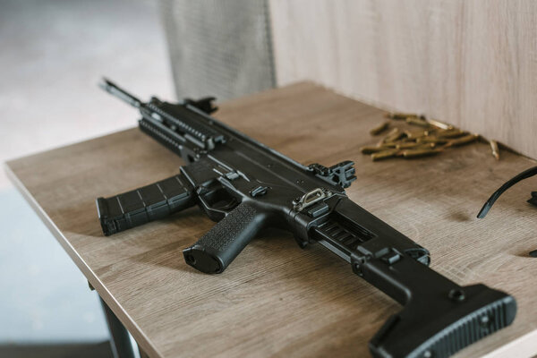 black rifle with bullets on wooden table in shooting range