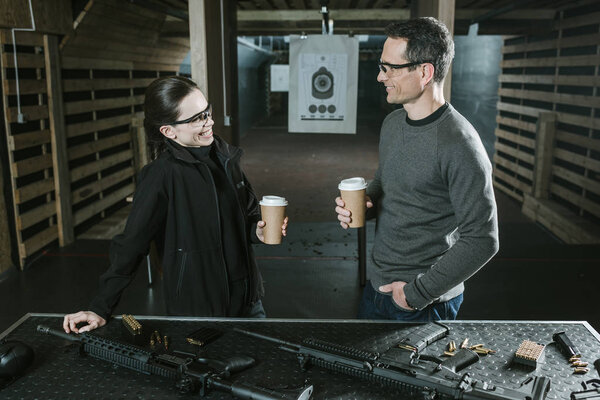 smiling customer and shooting instructor drinking coffee in shooting range