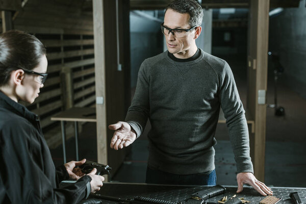 instructor showing gun to female client in shooting range 