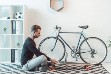 katta oturan ve kaykay üzerinde dizüstü kullanarak genç işadamı yan görünüm