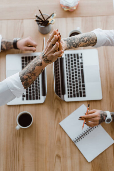 обрезанный снимок коллег, дающих пять во время работы с ноутбуками
