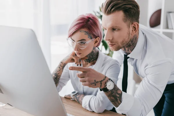 young tattooed business people in formal wear working with desktop computer in office