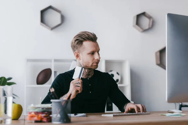 Young Tattooed Businessman Holding Credit Card Using Desktop Computer Workplace — Stock Photo, Image