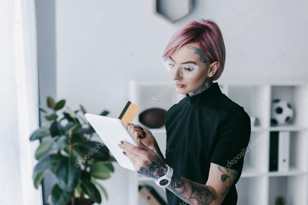 young tattooed businesswoman in eyeglasses holding credit card and using