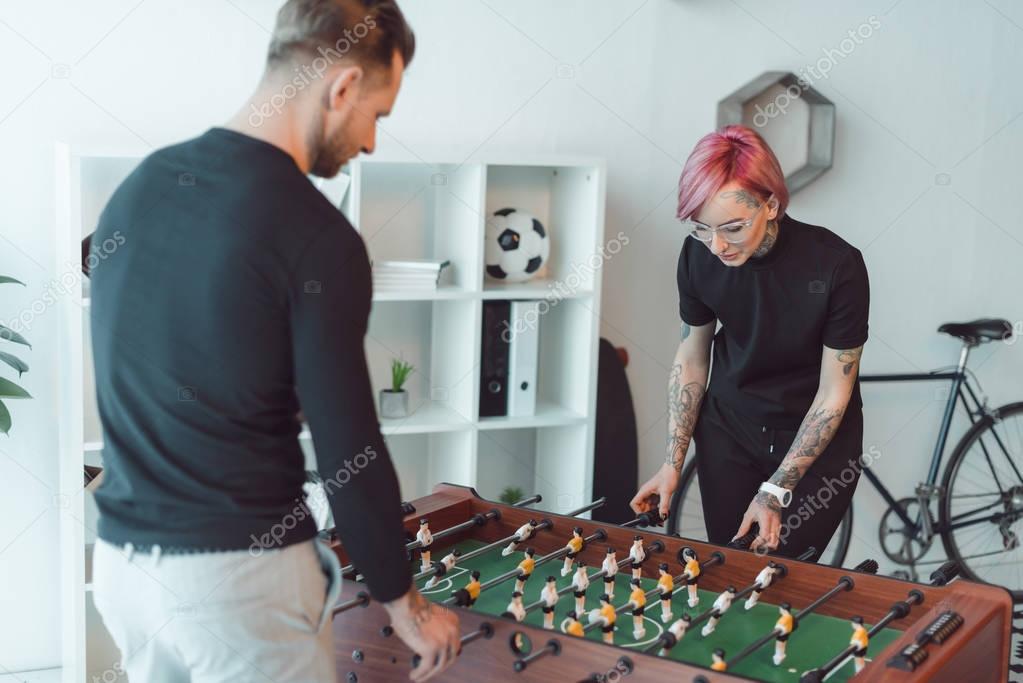 young tattooed colleagues playing foosball in office