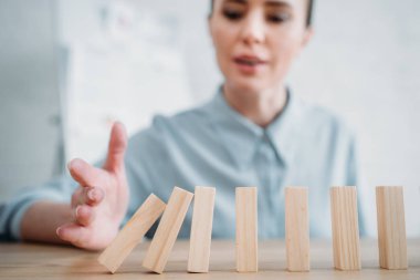 close-up shot of businesswoman with falling wooden blocks in row on table, dominoes effect concept clipart