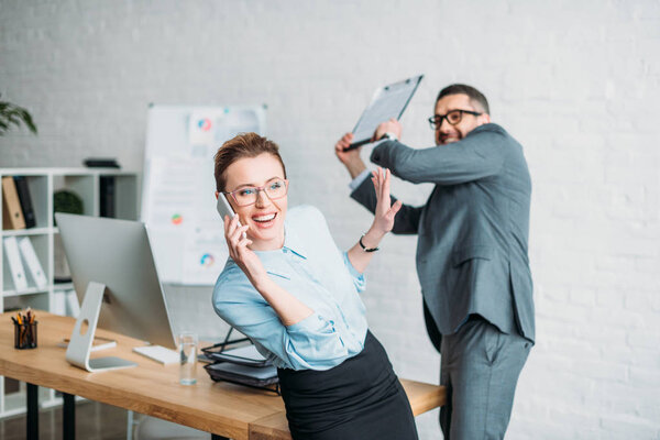 businessman get ready to hit his colleague with clipboard while she talking by phone and annoying him