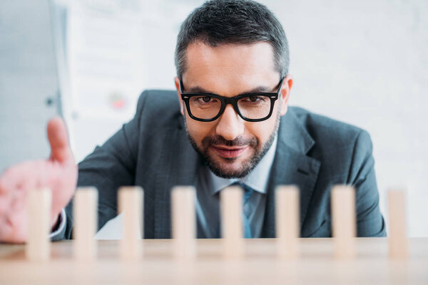 close-up shot of businessman assembling wooden blocks in row on worktable, dominoes effect concept