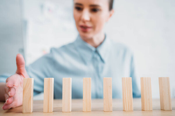 close-up shot of attractive businesswoman assembling wooden blocks in row on worktable, dominoes effect concept