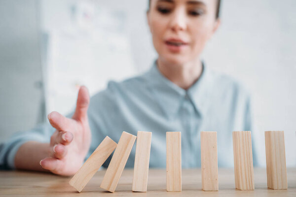 close-up shot of businesswoman with falling wooden blocks in row on table, dominoes effect concept