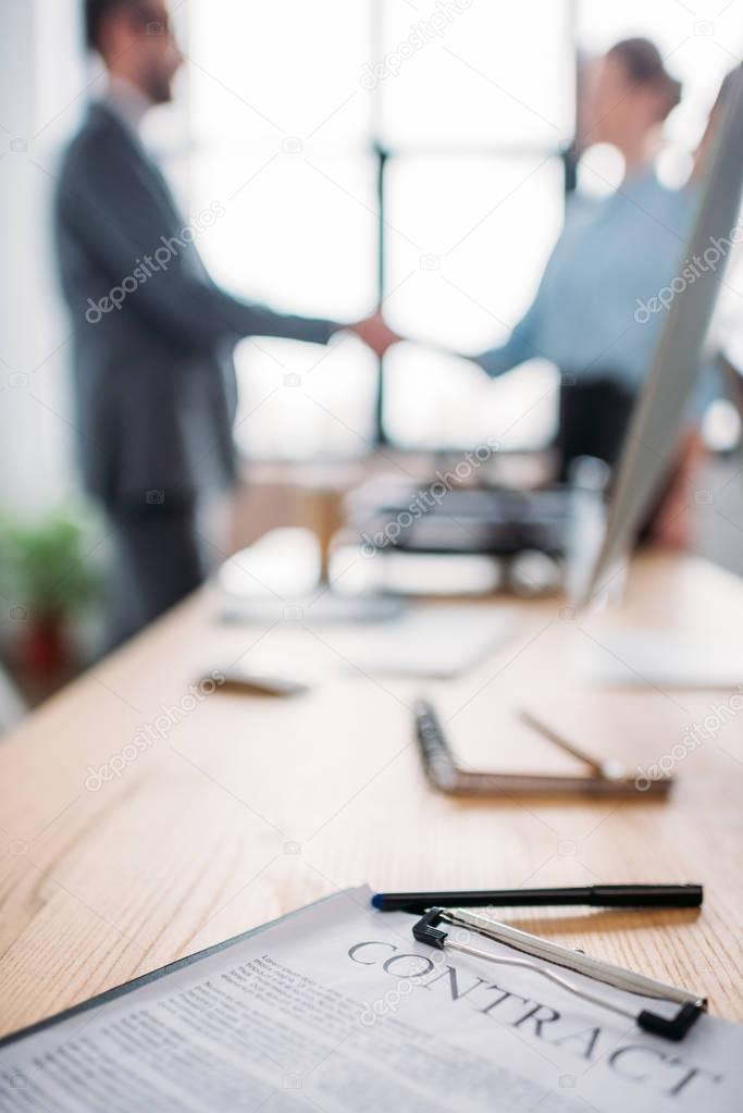 close-up shot of business contract lying on table and blurred business partners shaking hands on background