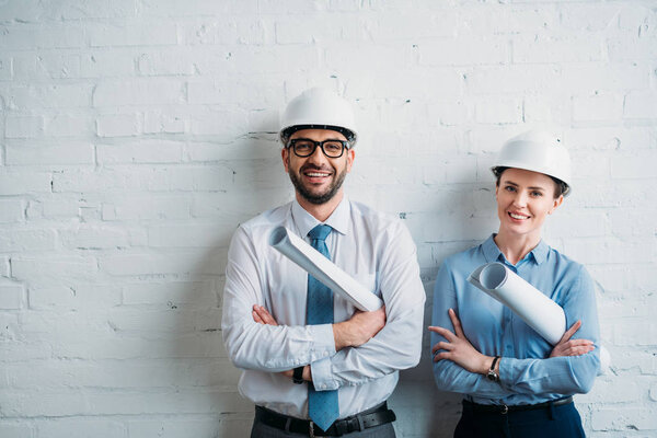 happy architects in hard hats standing in front of white brick wall with blueprints