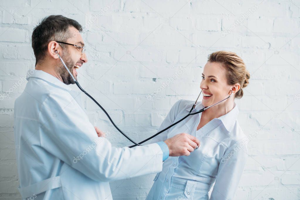 laughing doctors listening to heartbeat of each other with stethoscopes