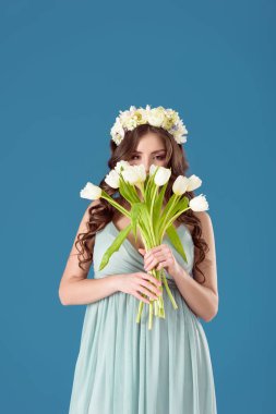 beautiful girl with flowers wreath on head sniffing tulips isolated on blue clipart