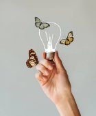 abgeschnittenes Bild einer Frau, die eine Lampe mit Schmetterlingen in der Hand hält, isoliert auf grau
