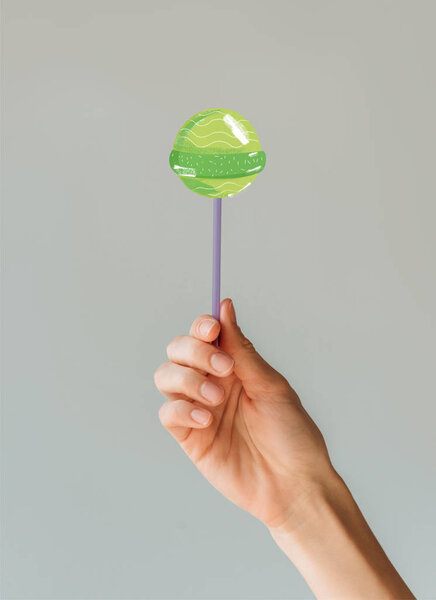 Cropped image of woman holding green lollipop in her hand isolated on gray 