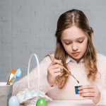 Чарівна маленька дівчинка малює великодні яйця за столом