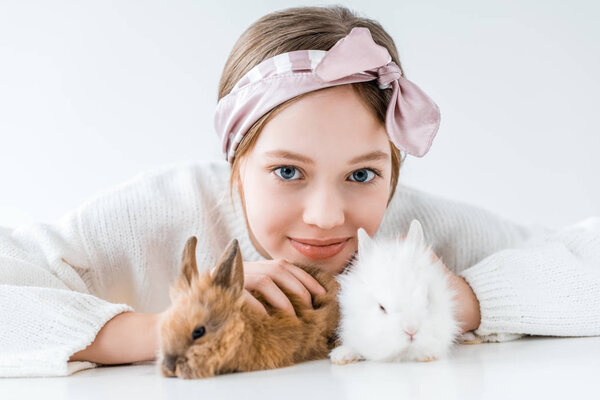 adorable little girl playing with rabbits and smiling at camera on white