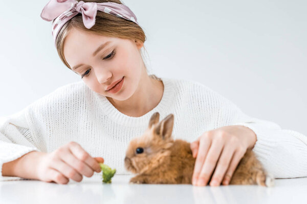 красивая улыбающаяся девушка кормит кролика брокколи на белом
