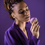 Sensual african american girl in purple jacket looking at cupcake, isolated on purple