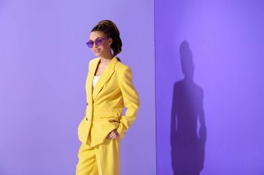 Sarı takım elbise ve trendy mor güneş gözlüğü, ultra violet arka plan üzerinde poz güzel melez kız