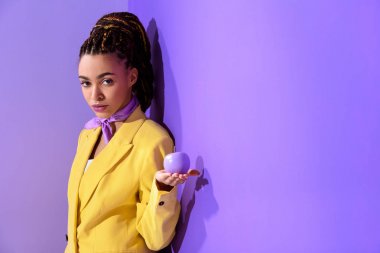 african american girl posing in yellow suit with purple apple, on trendy ultra violet background clipart