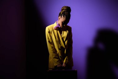 şık Afro-Amerikan kız karanlıkta trendy ultra violet zemin üzerine sarı elbiseli poz