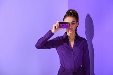 stylish beautiful mulatto girl in purple jacket taking photo on camera clipart