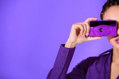 Cropped view of girl in purple jacket taking photo on camera, isolated on ultra violet clipart