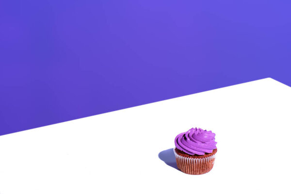 cupcake with purple buttercream glaze, on white surface 