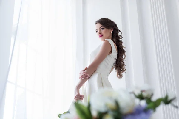 黑发白种新娘在婚礼礼服在窗口 花在前景 — 图库照片