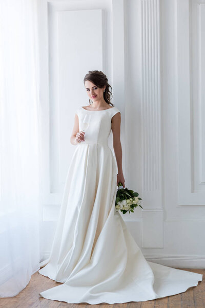 красивая невеста в традиционном платье со свадебным букетом и бокалом шампанского
