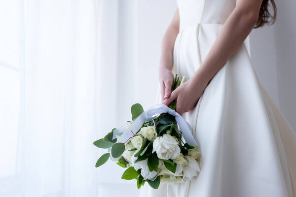 cropped view of bride in traditional dress holding wedding bouquet