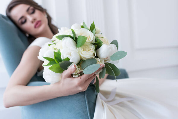 selective focus of bride with wedding bouquet sitting in armchair