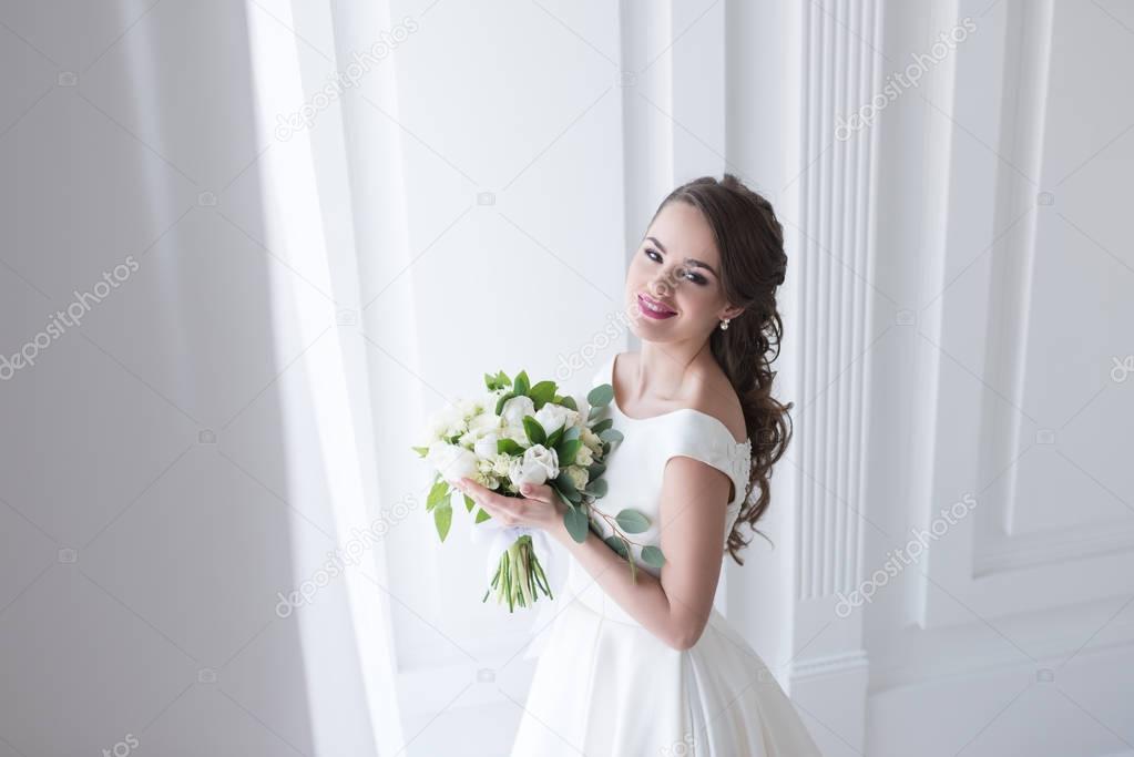 happy young bride posing in elegant white dress with wedding bouquet