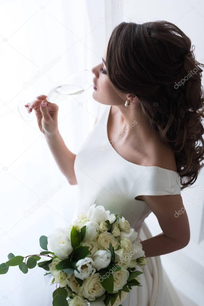beautiful young bride with wedding bouquet drinking champagne