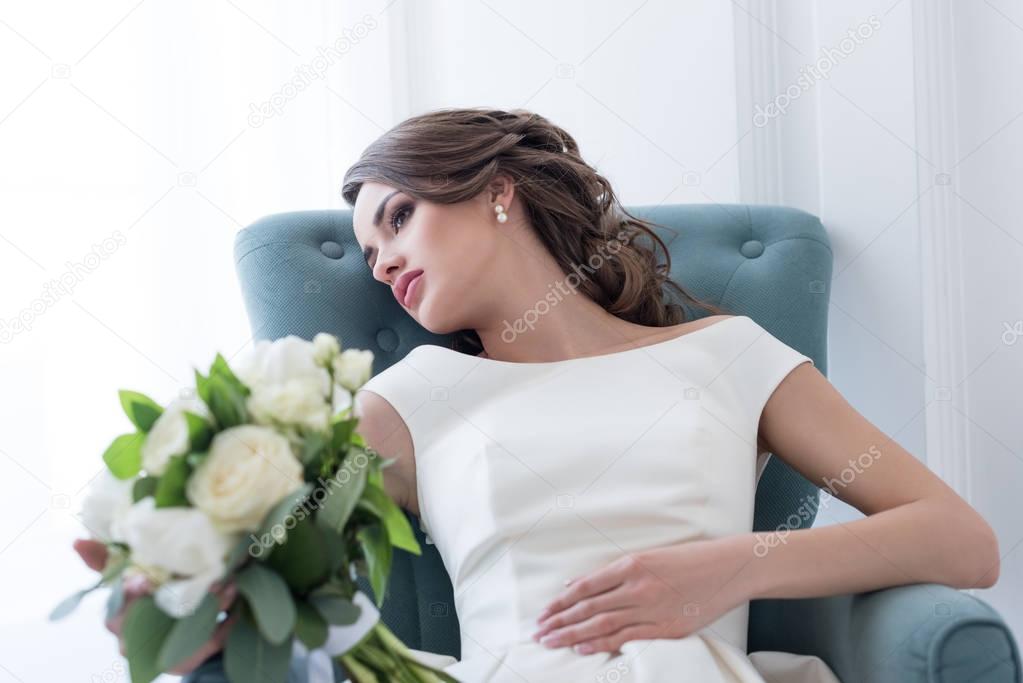 young bride with wedding bouquet sitting in armchair