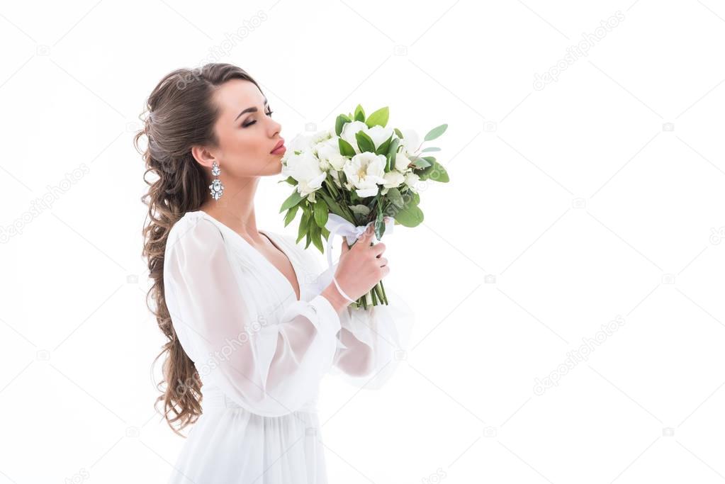 attractive bride in white dress sniffing wedding bouquet, isolated on white