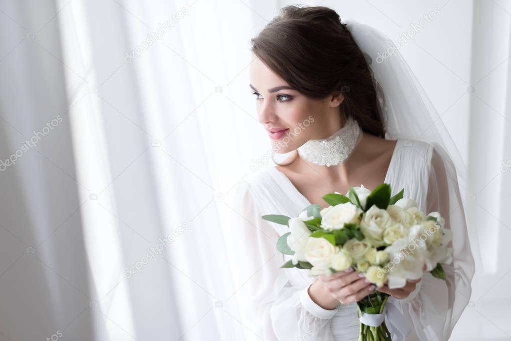 smiling bride in wedding dress and veil holding white bouquet