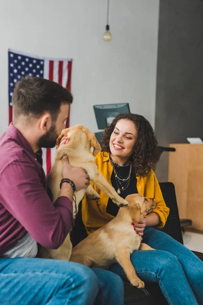 男と女の つのラブラドール子犬が付いているソファーの上に座って  — 無料ストックフォト